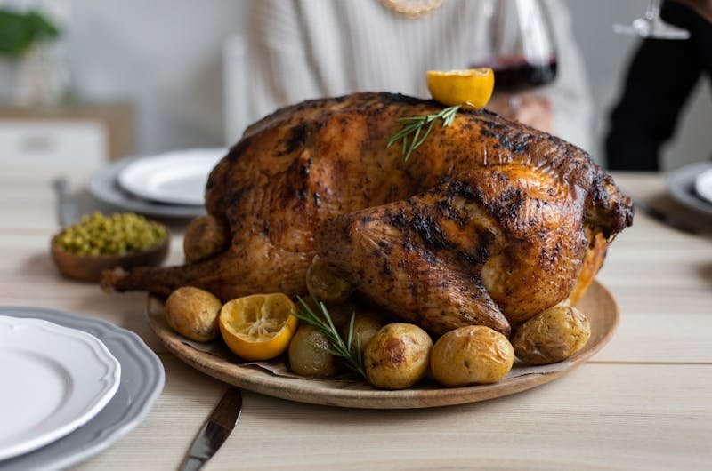 From above of big turkey roasted with lemon and potatoes on round wooden tray placed on table for celebrating Thanksgiving Day