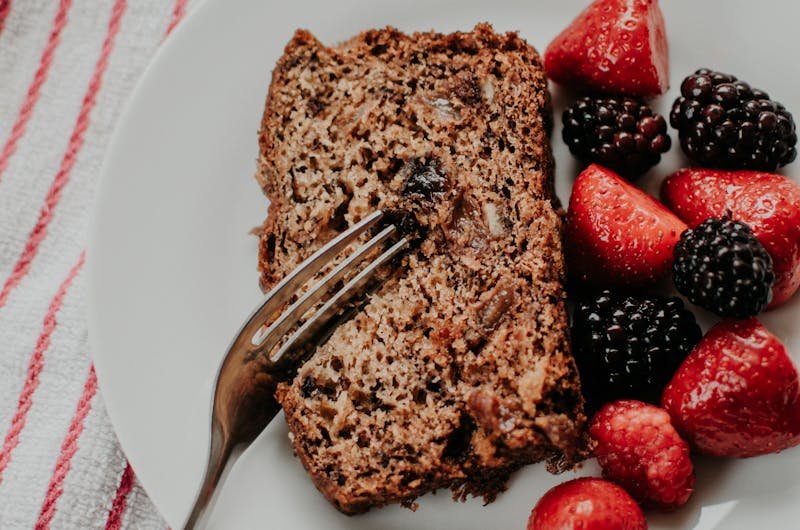 Slice of banana bread served with fresh strawberries and blackberries on a white plate.