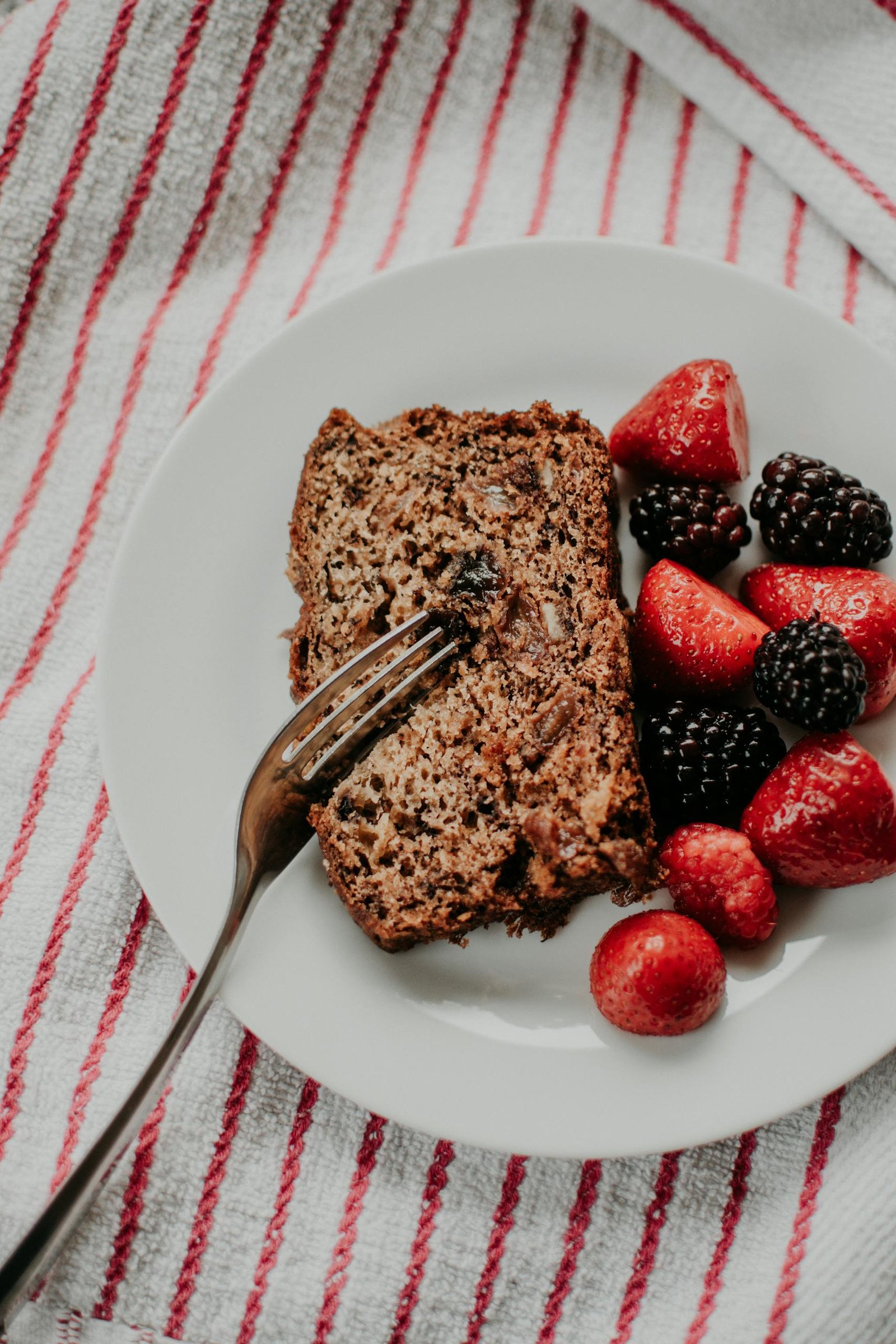Slice of banana bread served with fresh strawberries and blackberries on a white plate.