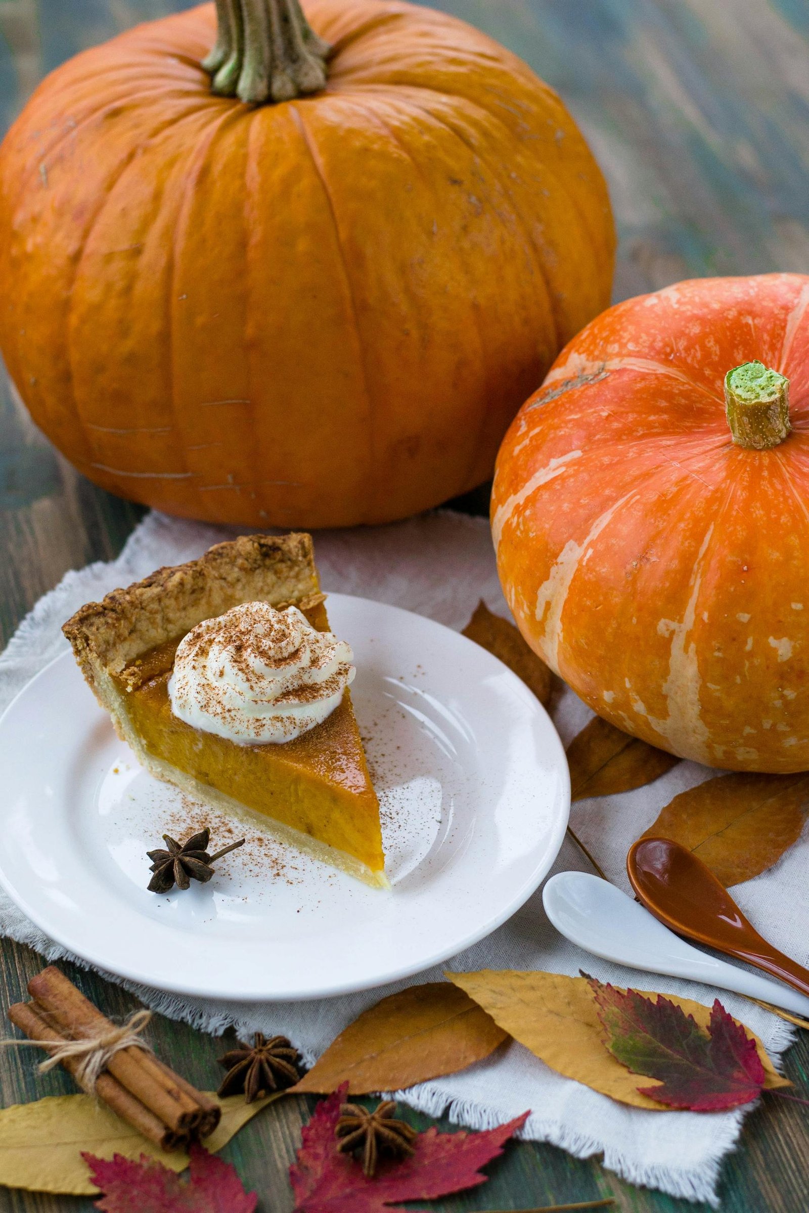 Slice of pumpkin pie with whipped cream, surrounded by pumpkins and autumn leaves, perfect for fall celebrations.